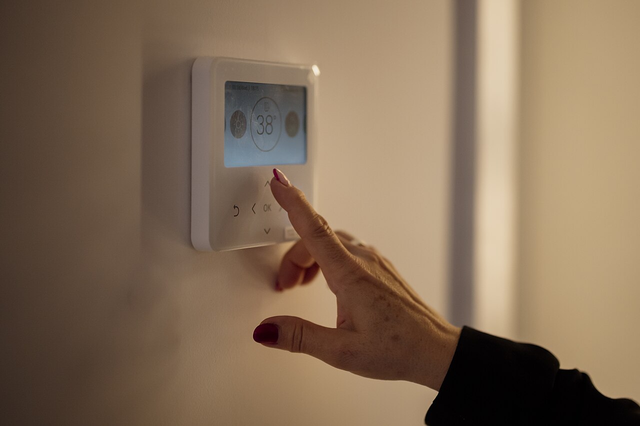 Main réglant un thermostat mural dans un logement